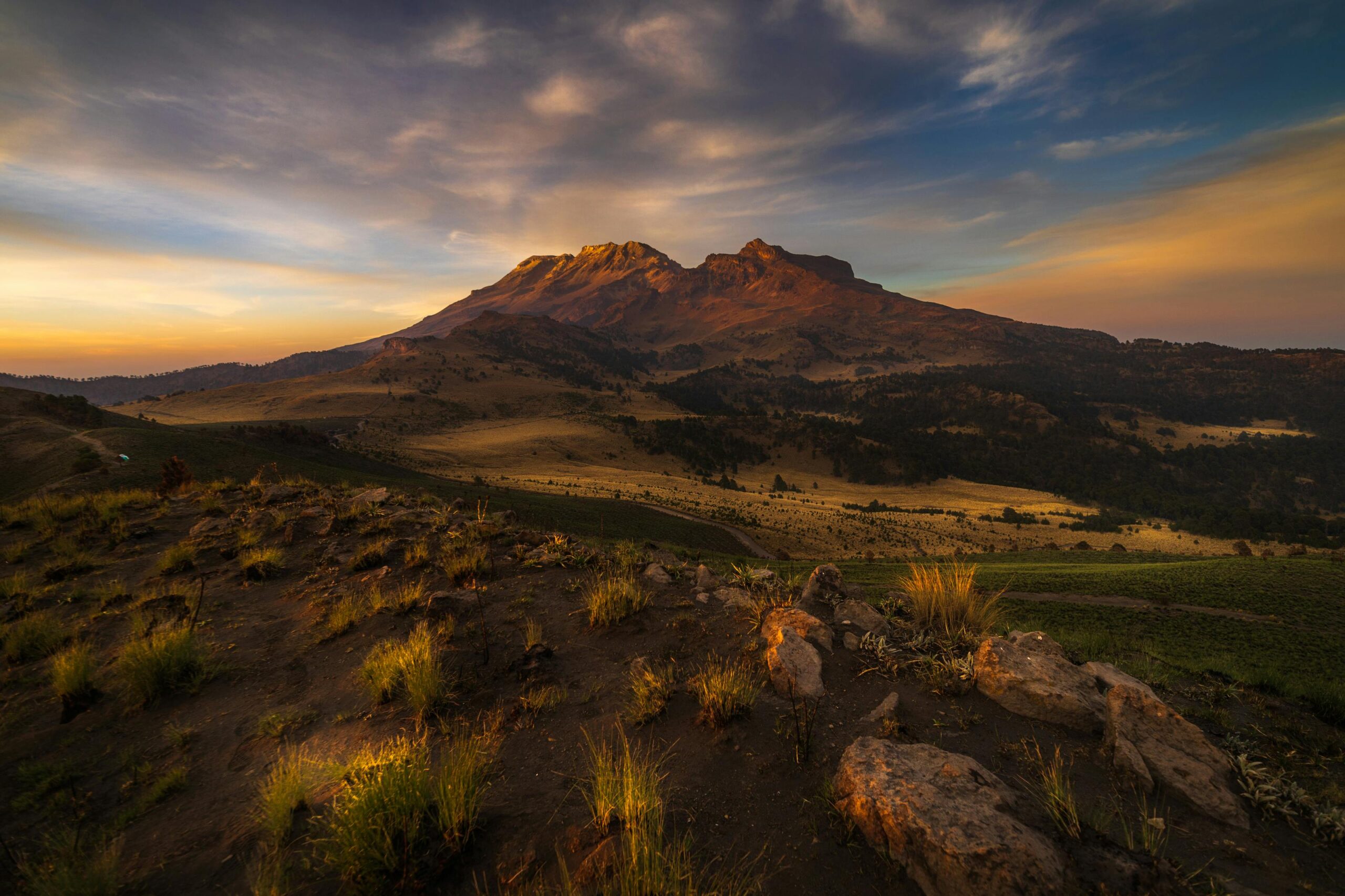 Breathtaking sunset view of Izta-Popo mountains in Mexico, featuring vibrant sky and lush landscape.