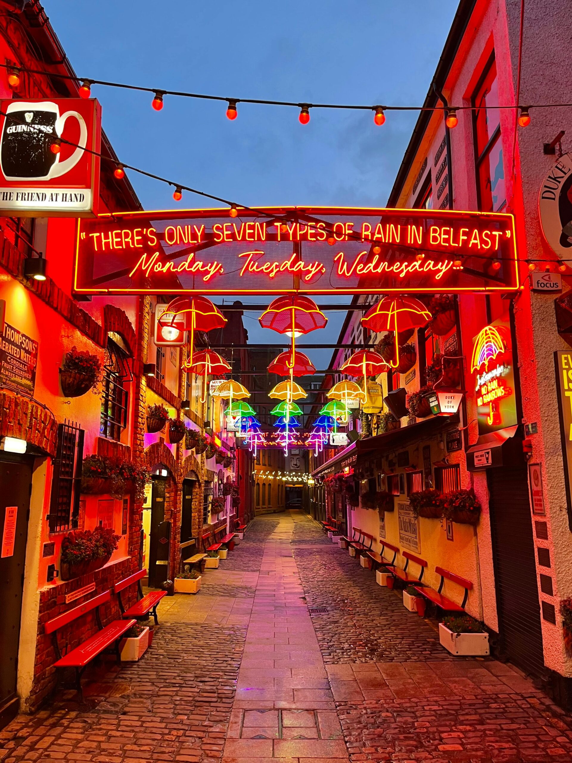 Illuminated street in Belfast with neon signs and colorful umbrellas.