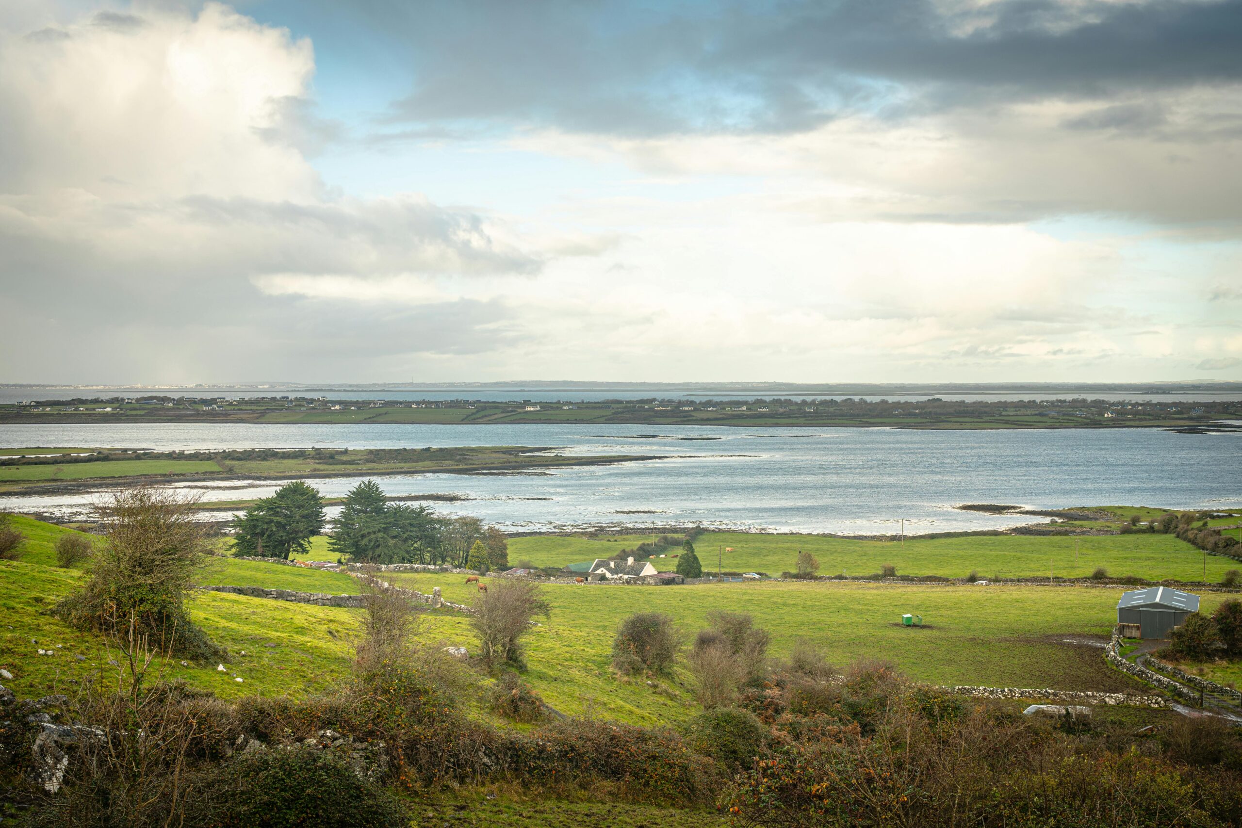 Lush green landscape of Burren, Ireland with tranquil lakes under a cloudy sky.